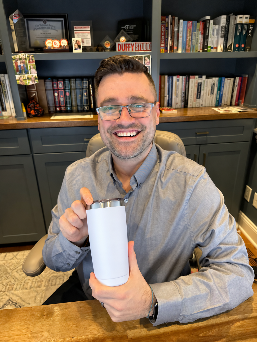 Sean smiling at his desk, with books and career mementos behind him